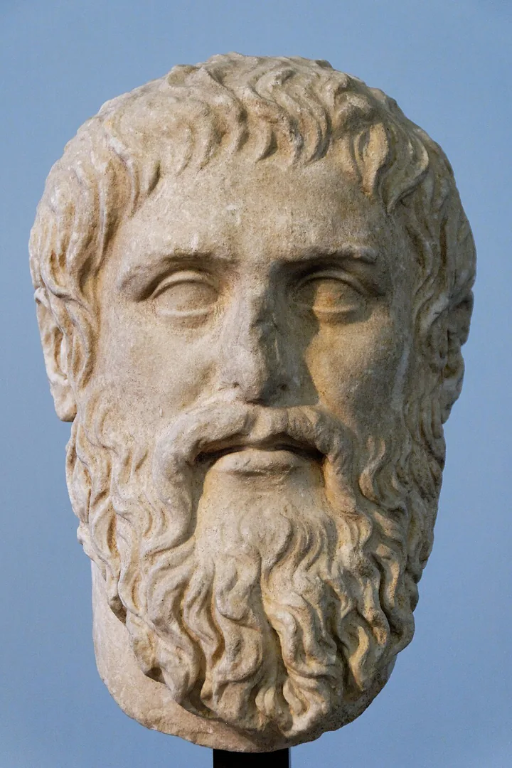 Frontal view of a marble portrait head identified as Plato, with a full beard, against a blue background.